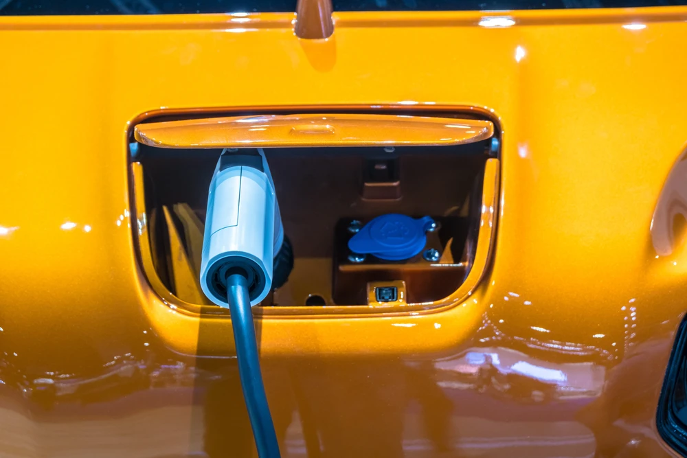 Extérieur automobile, véhicule électrique en cours de recharge. Un câble de charge bleu est connecté au port situé dans un compartiment ouvert sur la carrosserie jaune brillante.
